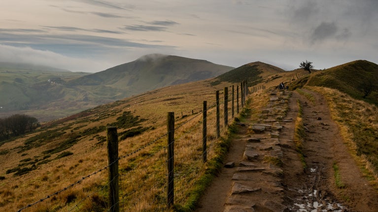 A footpath alongside a wire fence through a moody landscape with hills in the distance